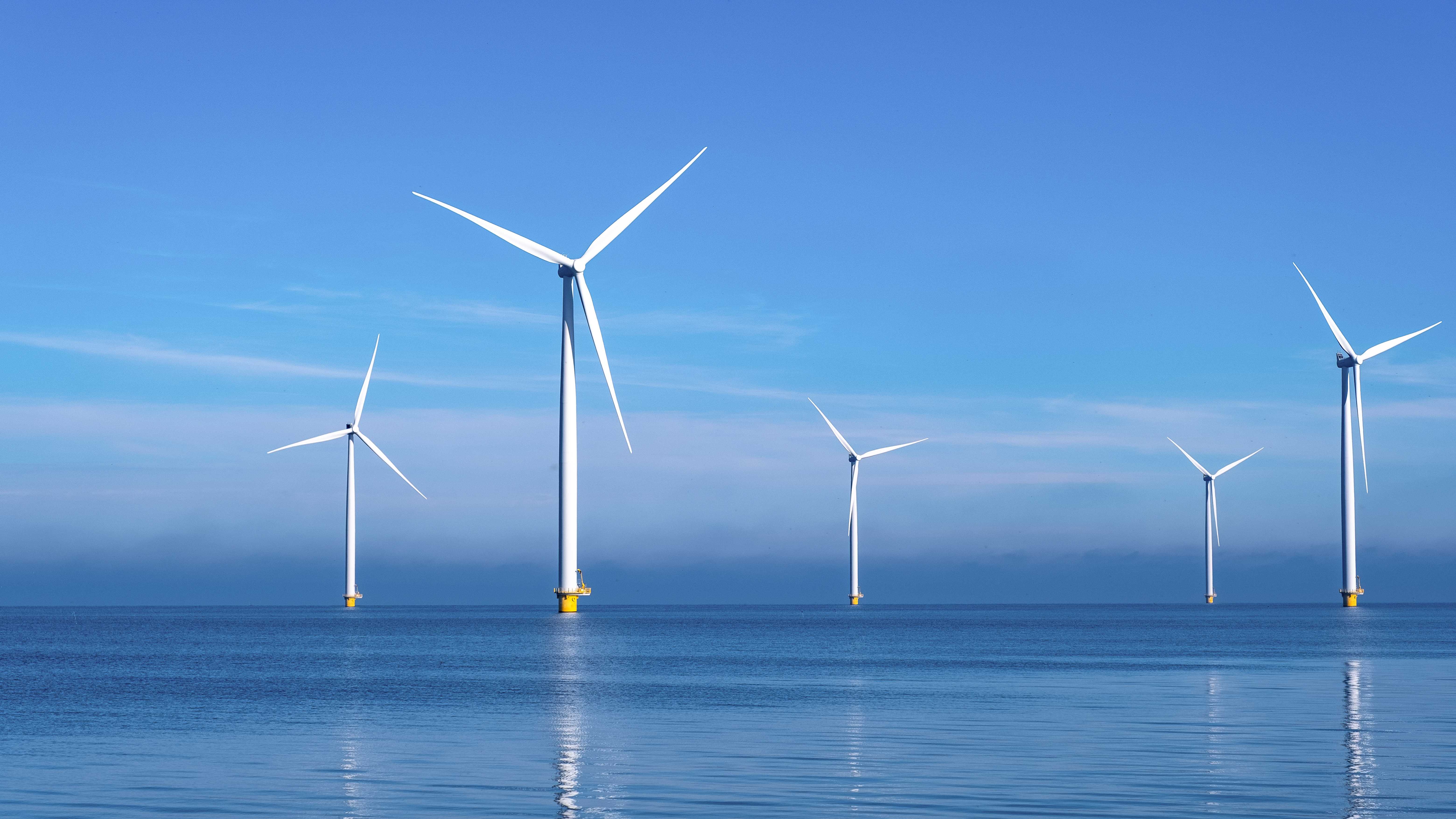 Offshore wind turbines stand tall in calm blue sea under a clear sky. The serene environment and clean energy symbols evoke a sense of tranquility and sustainability.