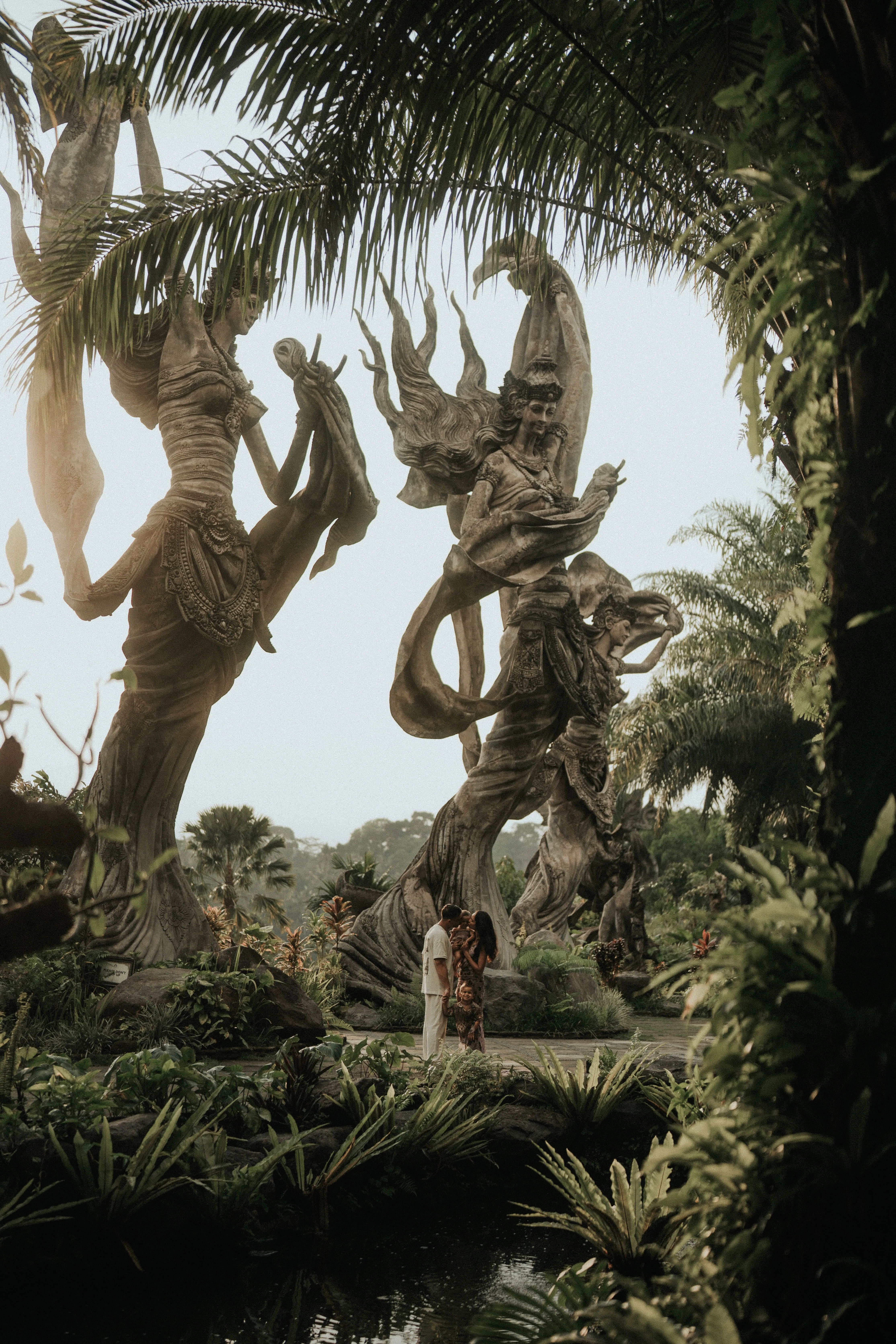 Couple poses near mystical wooden sculptures in lush tropical garden