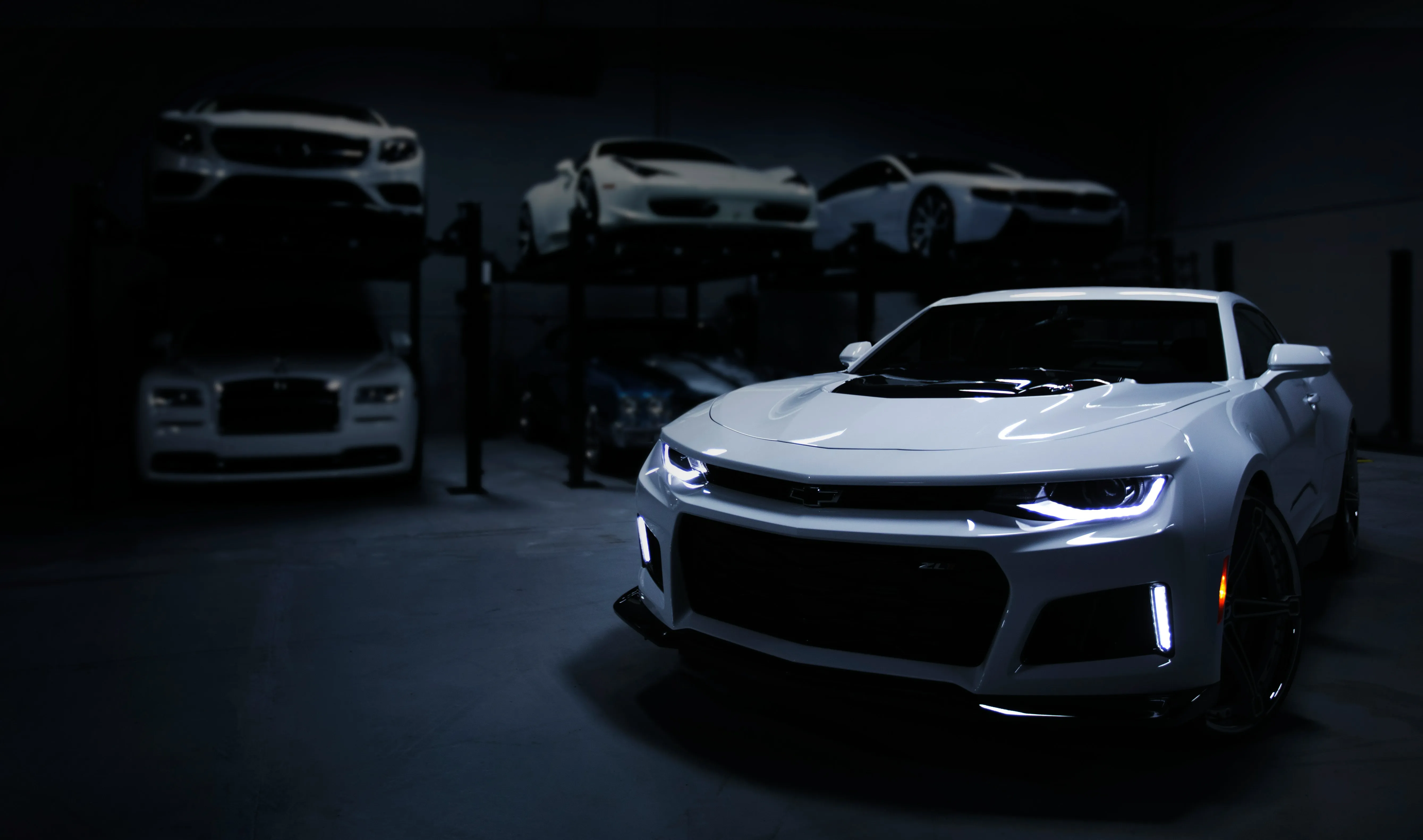 Front-angle view of a white muscle car in a dark showroom