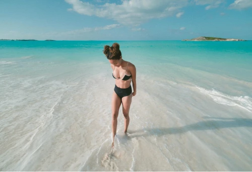 A woman posing for a picture as the sea water runs over her feet.