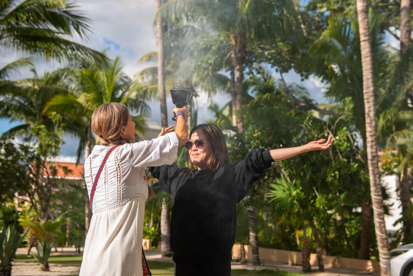 One woman sprays smoke on another woman's head outdoors.