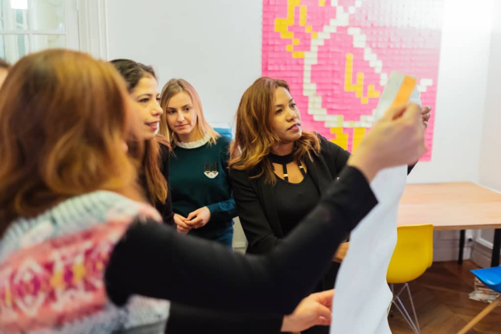 Quatre professionnelles en atelier, l'une d'elles présentant une feuille au groupe