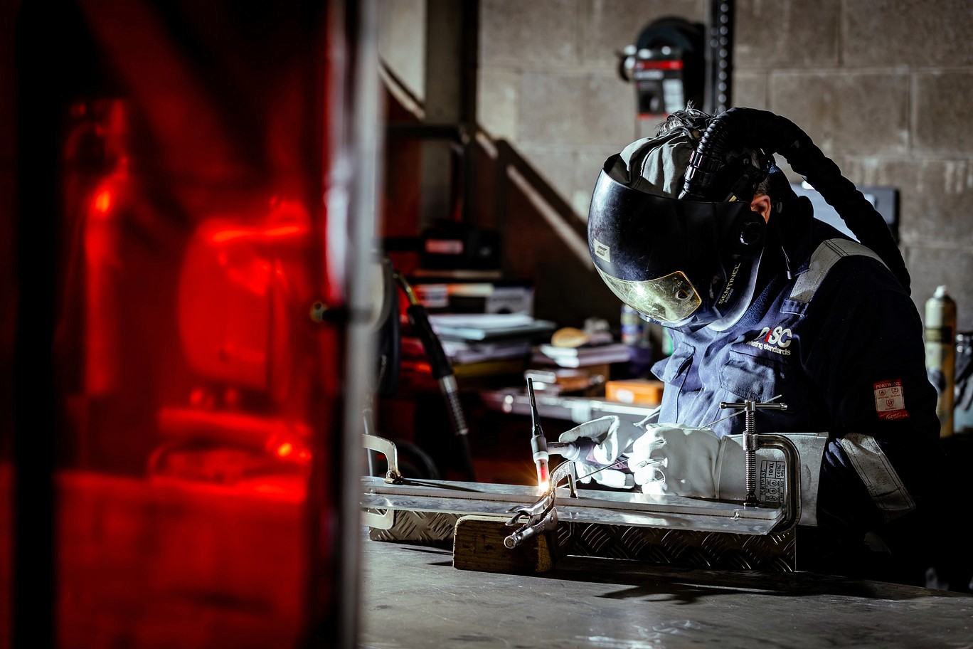 CASC employee welding a metal component in a workshop, wearing protective gear and working at a fabrication bench.