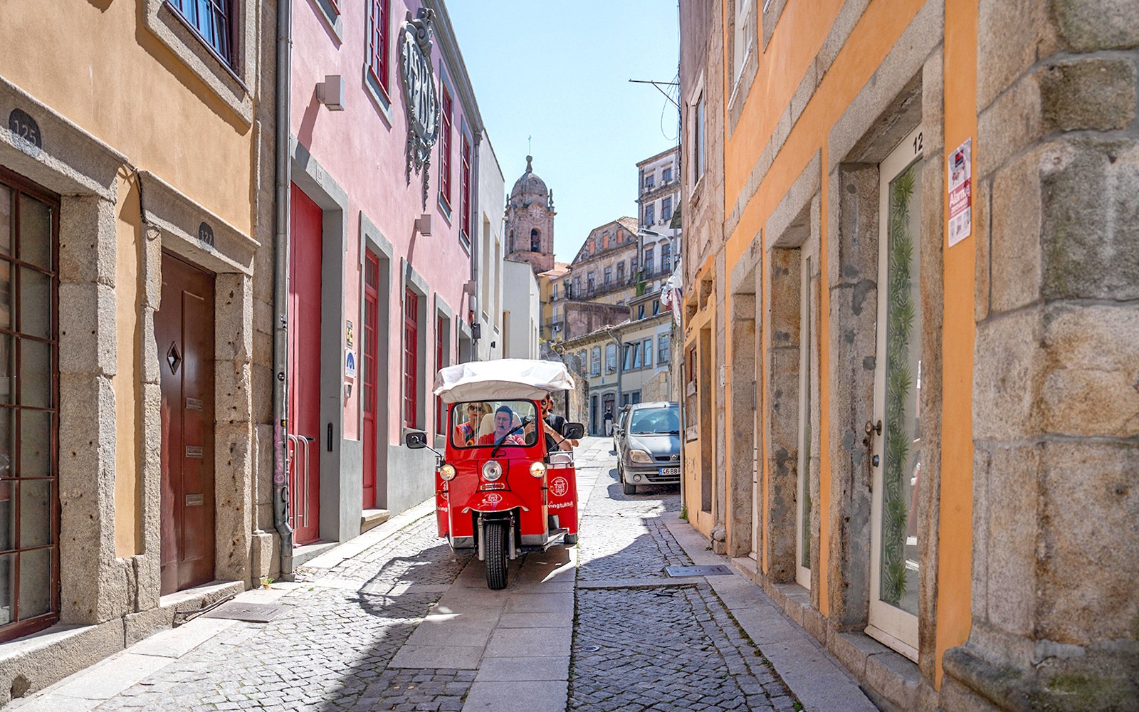 Tuk-tuk eléctrico en una calle estrecha de Oporto, Portugal, con edificios coloridos.