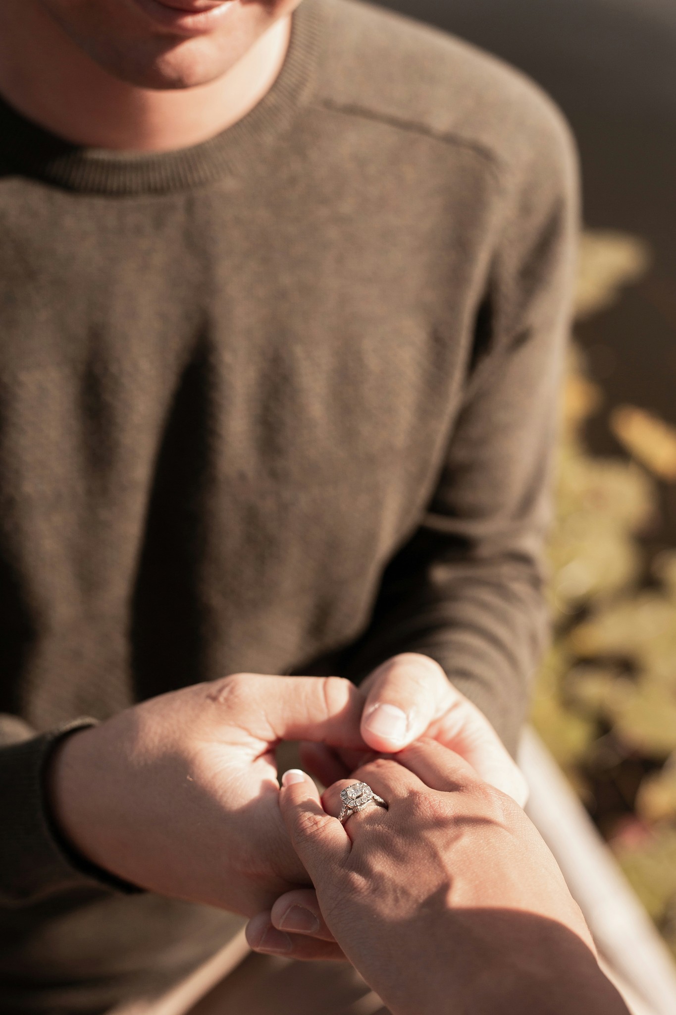 Couple holding hands with a diamond engagement ring catching the warm sunlight during an outdoor session
