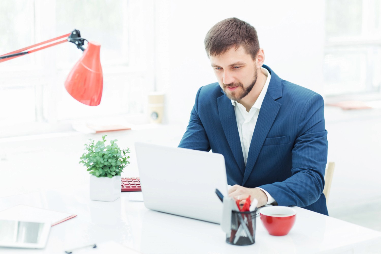  A man in a suit focused on his laptop, engaged in professional work in a modern office setting.