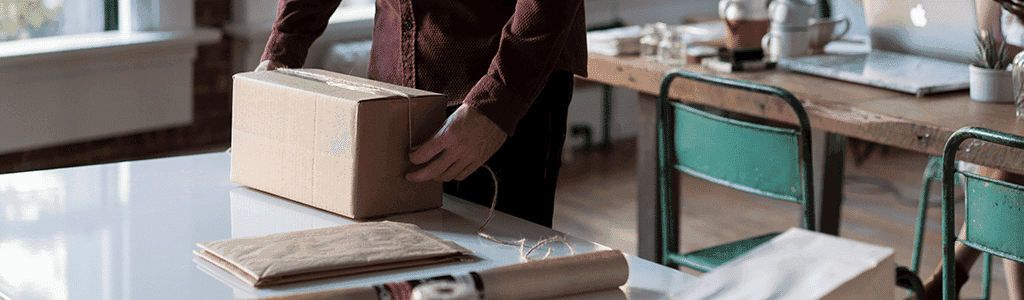 man packs a parcel on a desk - How to Ship Internationally