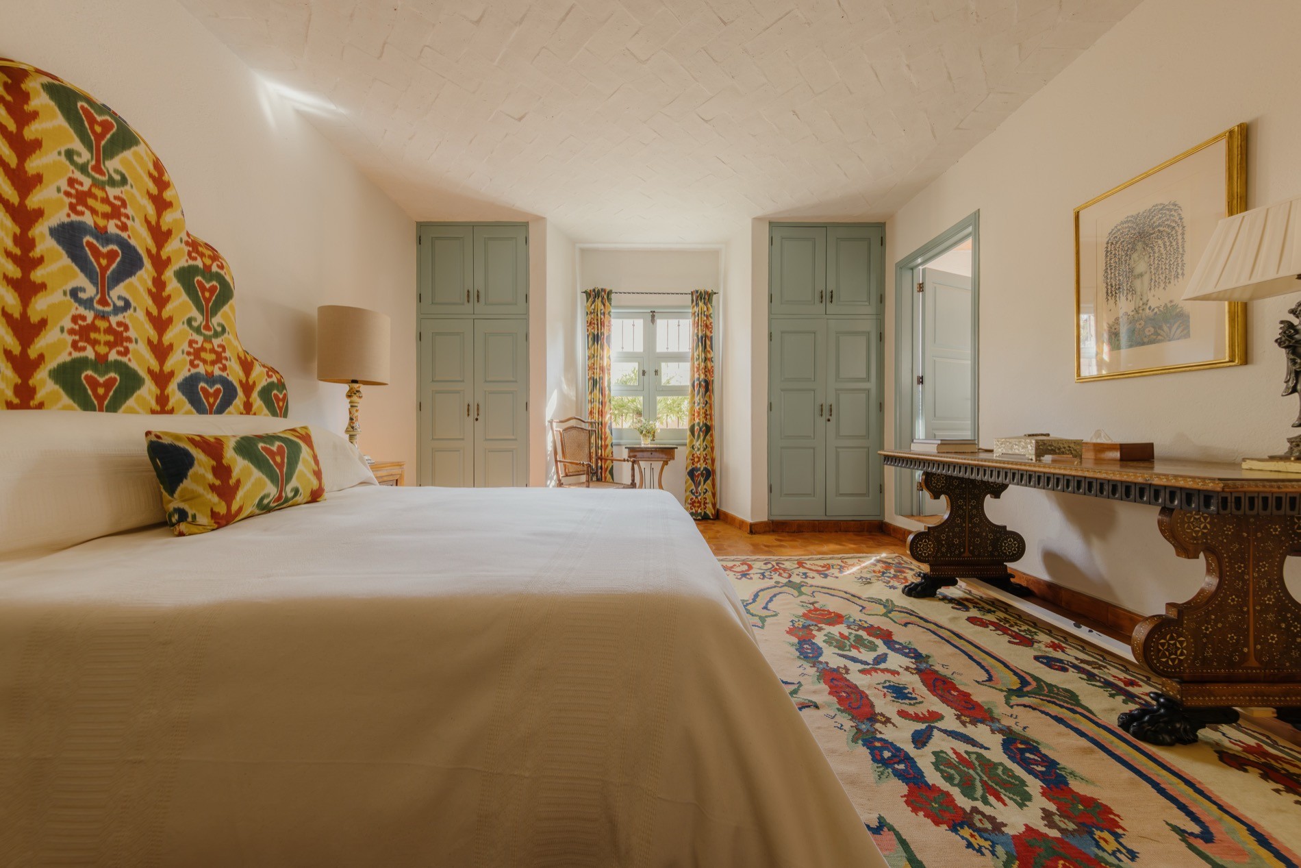 La Residencia guest bedroom with ikat bed, floral needlepoint rug, and whitewashed ceiling