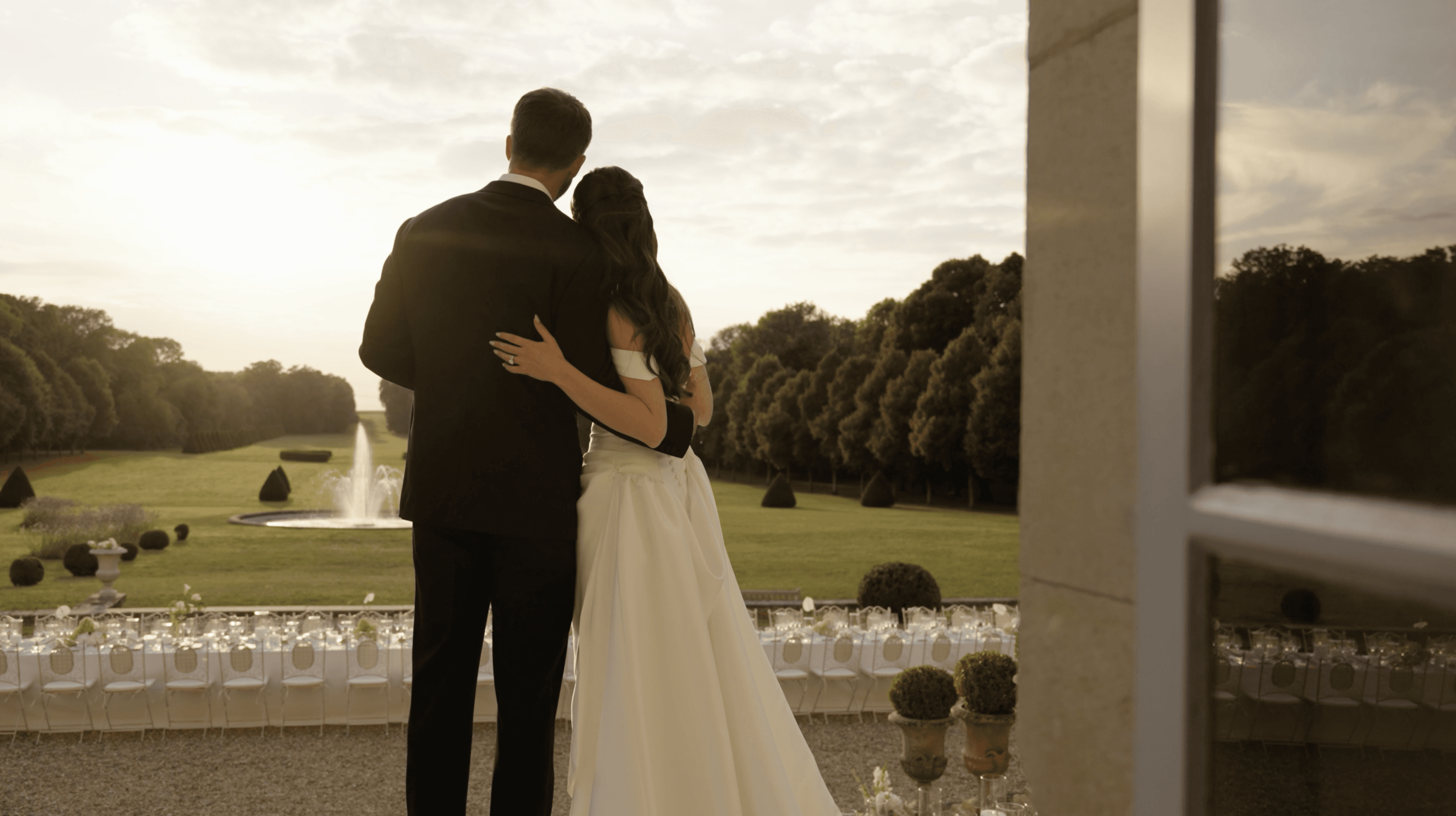 Couple hugging as they overlook their dining setting at their wedding. During sunset 