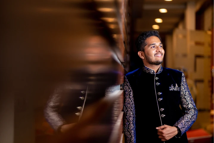 Jashwanth in a dark blue sherwani, posing elegantly in a lavish setting. Captured by Out of The Blues Fine Art Wedding Photography in Hyderabad.