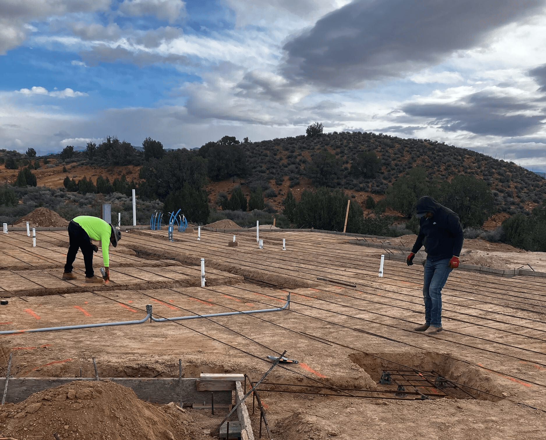 Jobsite in Leeds, Utah with footings dug and rebar being laid by workers with the stunning Southern Utah landscape in the background.