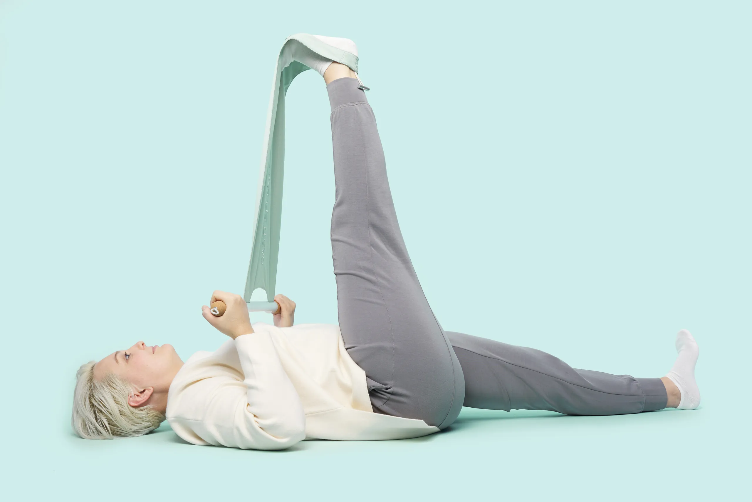 Person using CastleFlexx to stretch one leg while lying on a light blue background