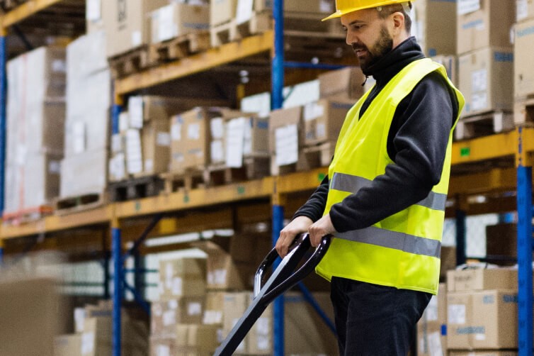 Warehouse worker in safety vest and helmet moving boxes