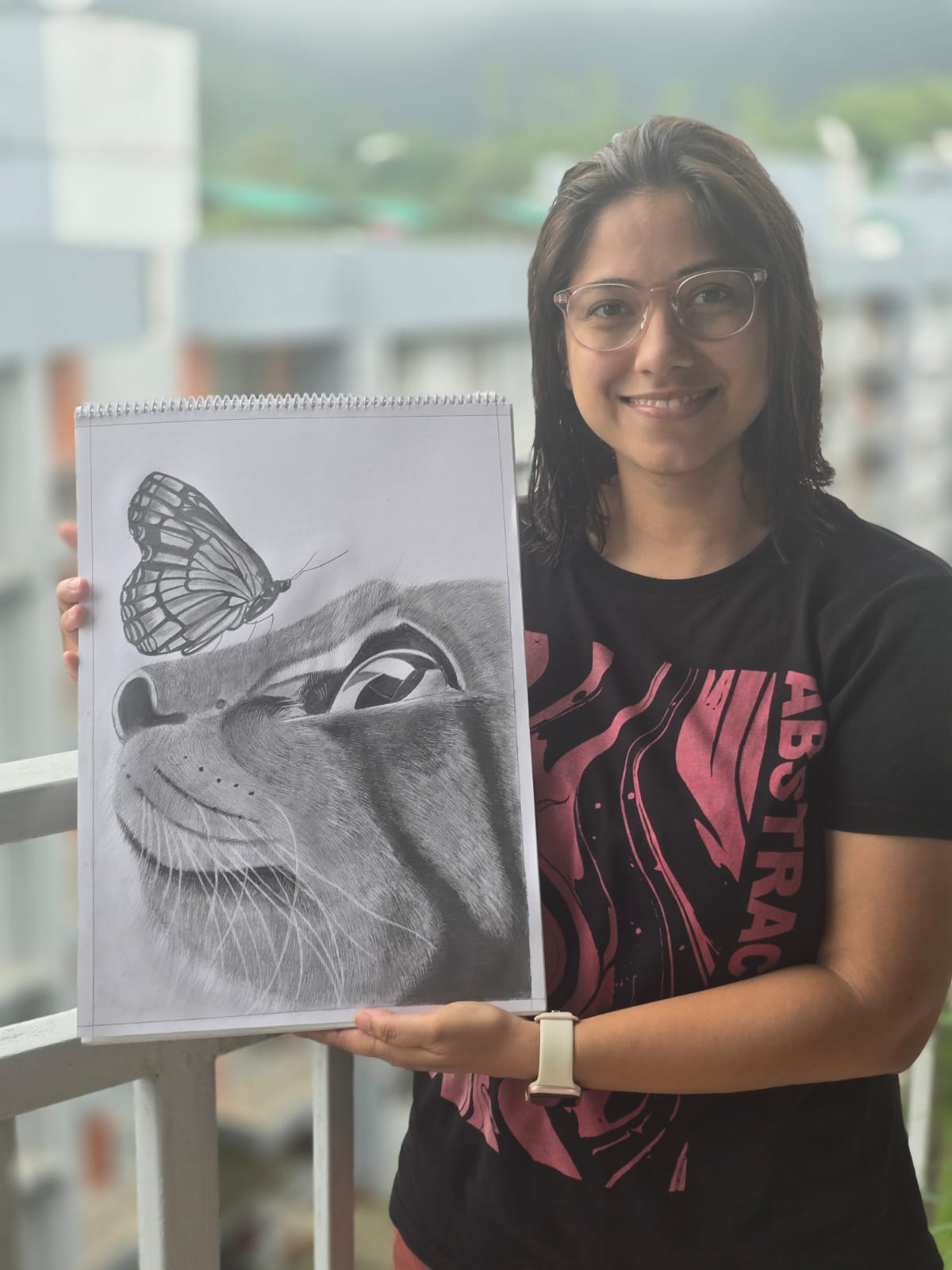 A person holding a detailed pencil sketch of a cat and a butterfly sitting on the cat's nose, in the Creative Pod studio.