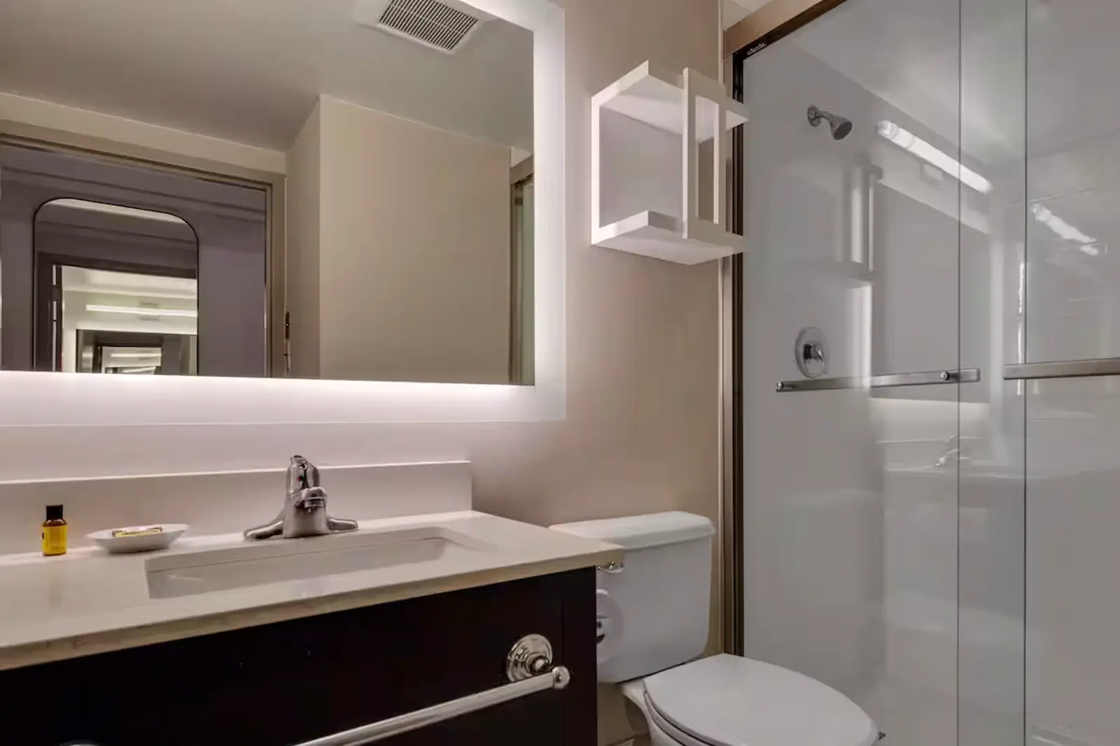 Modern bathroom with dark vanity, illuminated mirror, toilet, and shower.