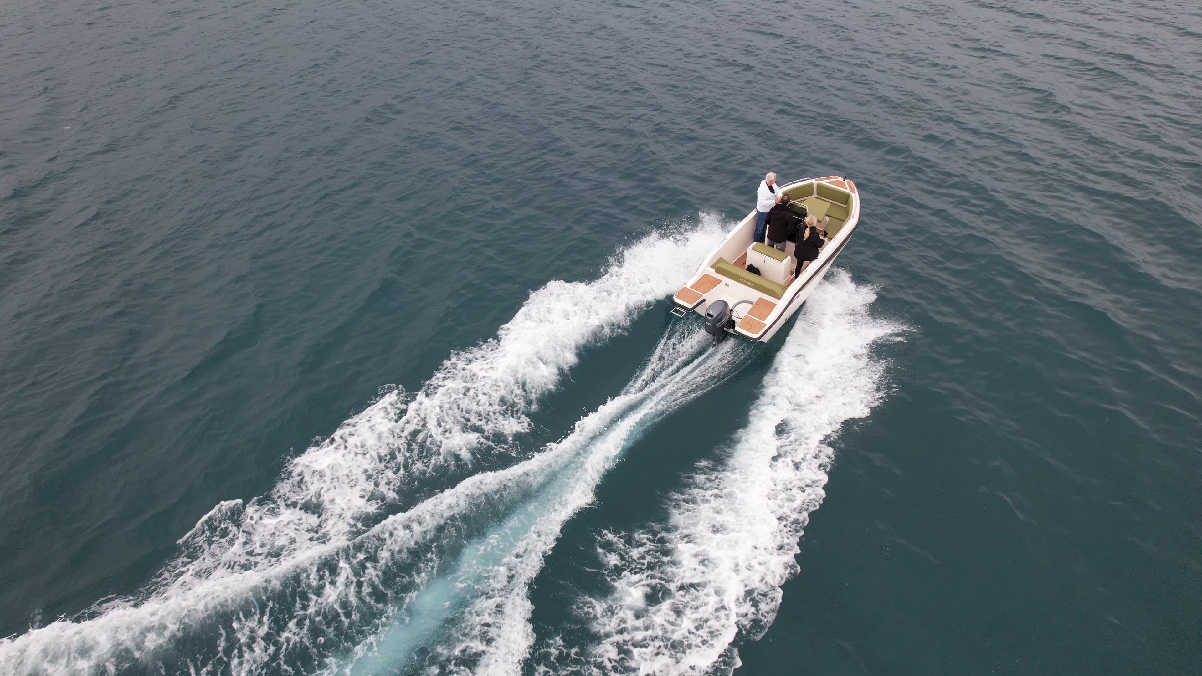 Small open speedboat with wooden deck cruising through turquoise waters, creating white wake trails behind it.
