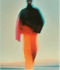 A man in a bright orange and black jacket walks along a sandy beach, with waves gently lapping at the shore.