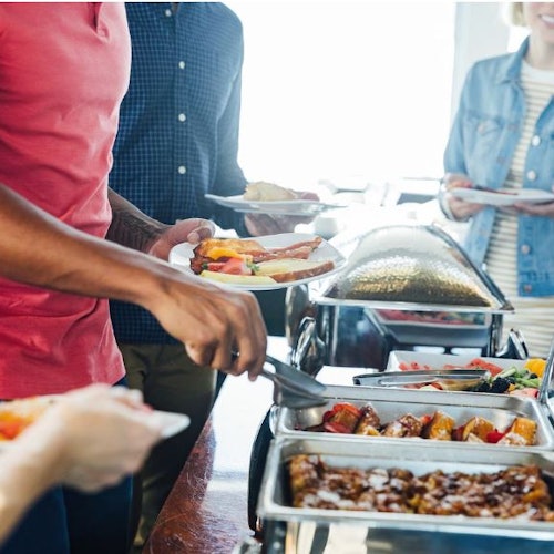 人们在自助餐台上自己取食物,手持餐盘并使用餐具盛取食物。