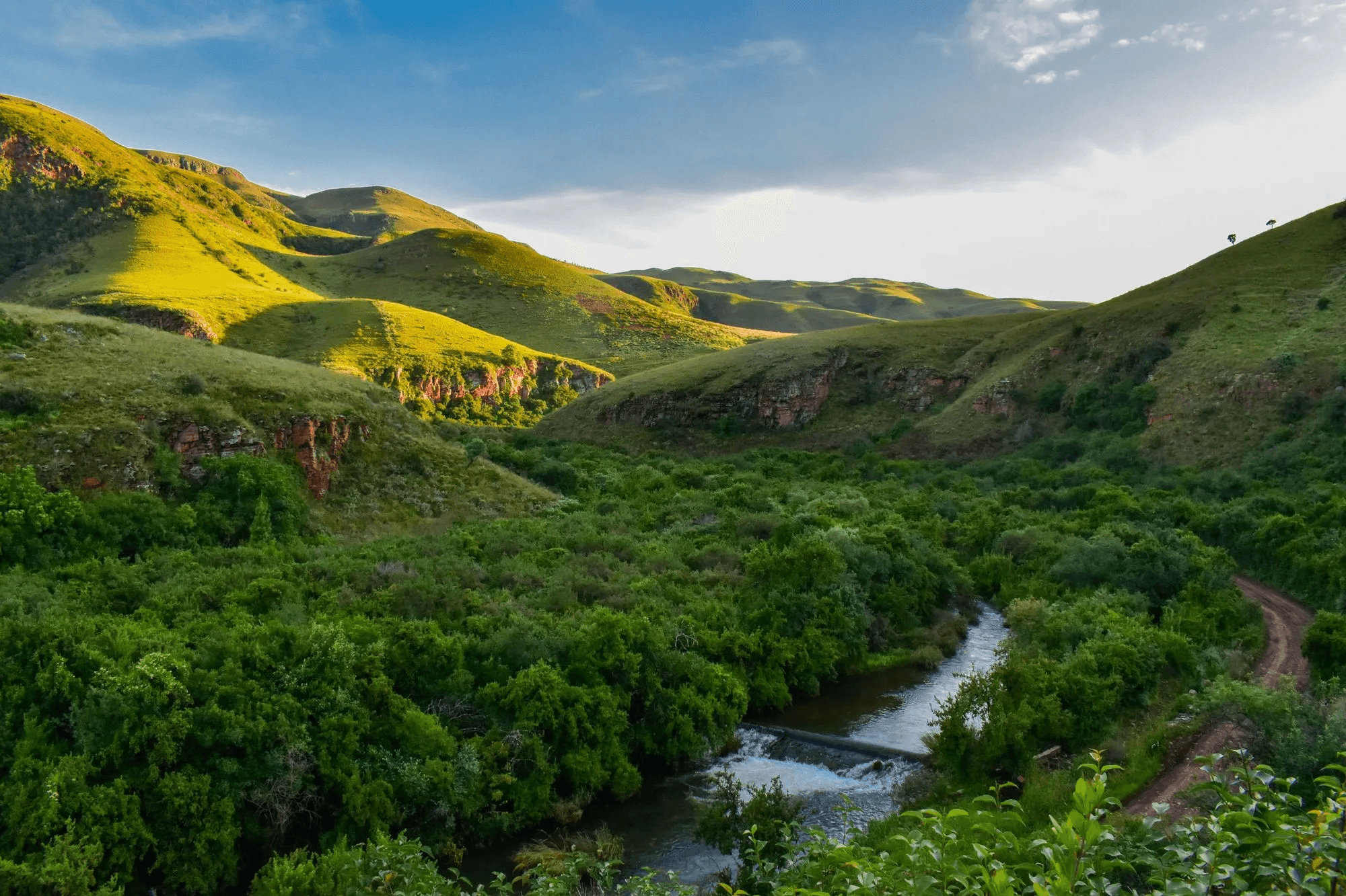 Lush green mountains by a dirt road and creek in Mpumalanga