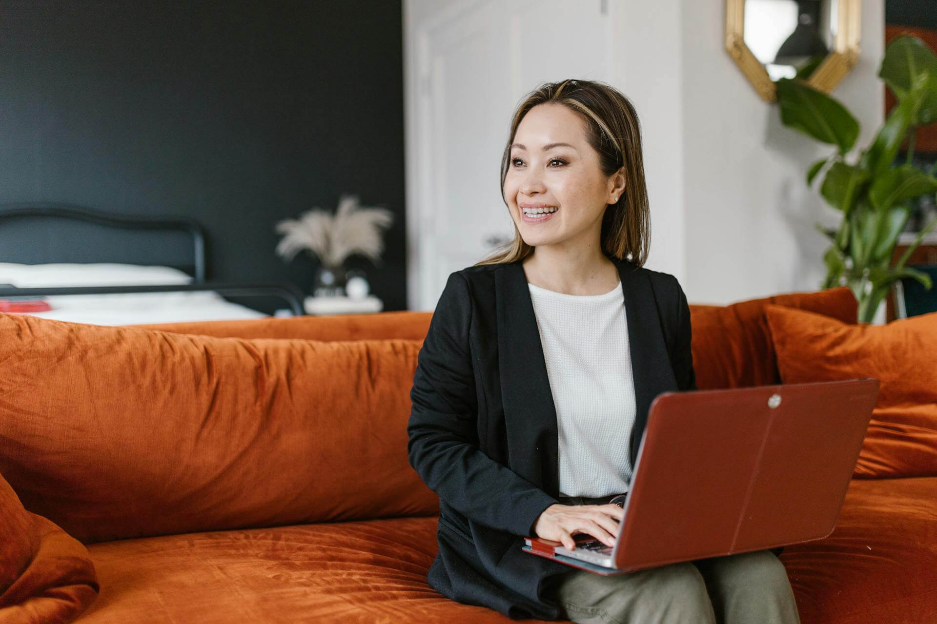 a women sitting on an orange sofa with laptop on her lap
