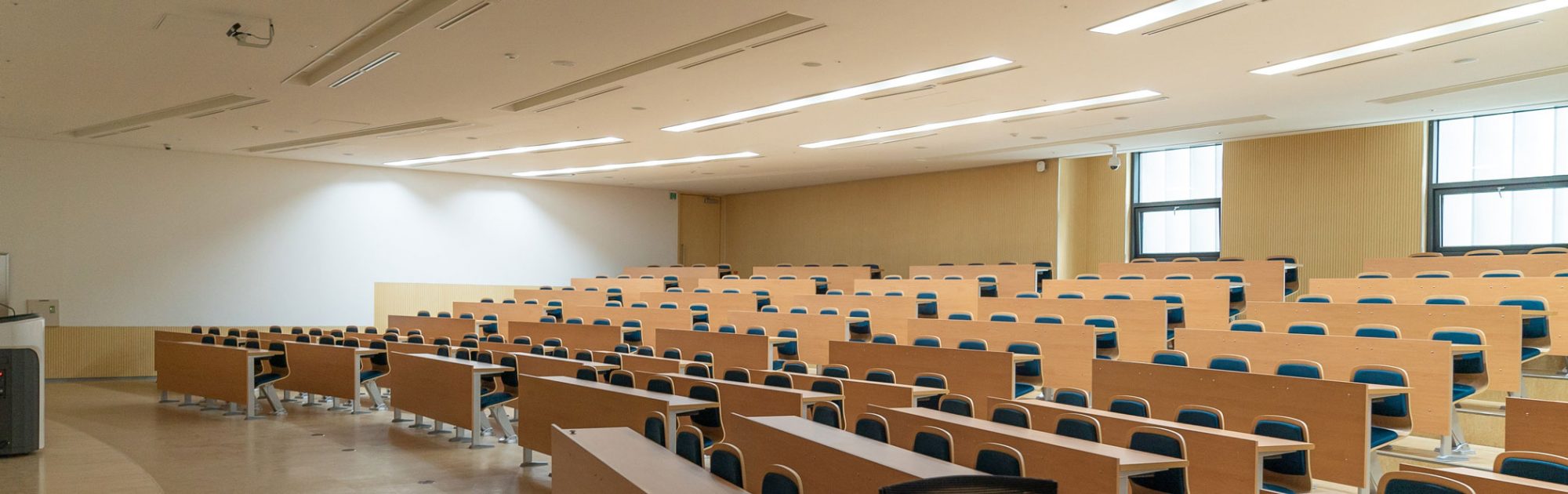 Rows of empty chairs in a large, well-lit conference room with wooden walls and a high ceiling.