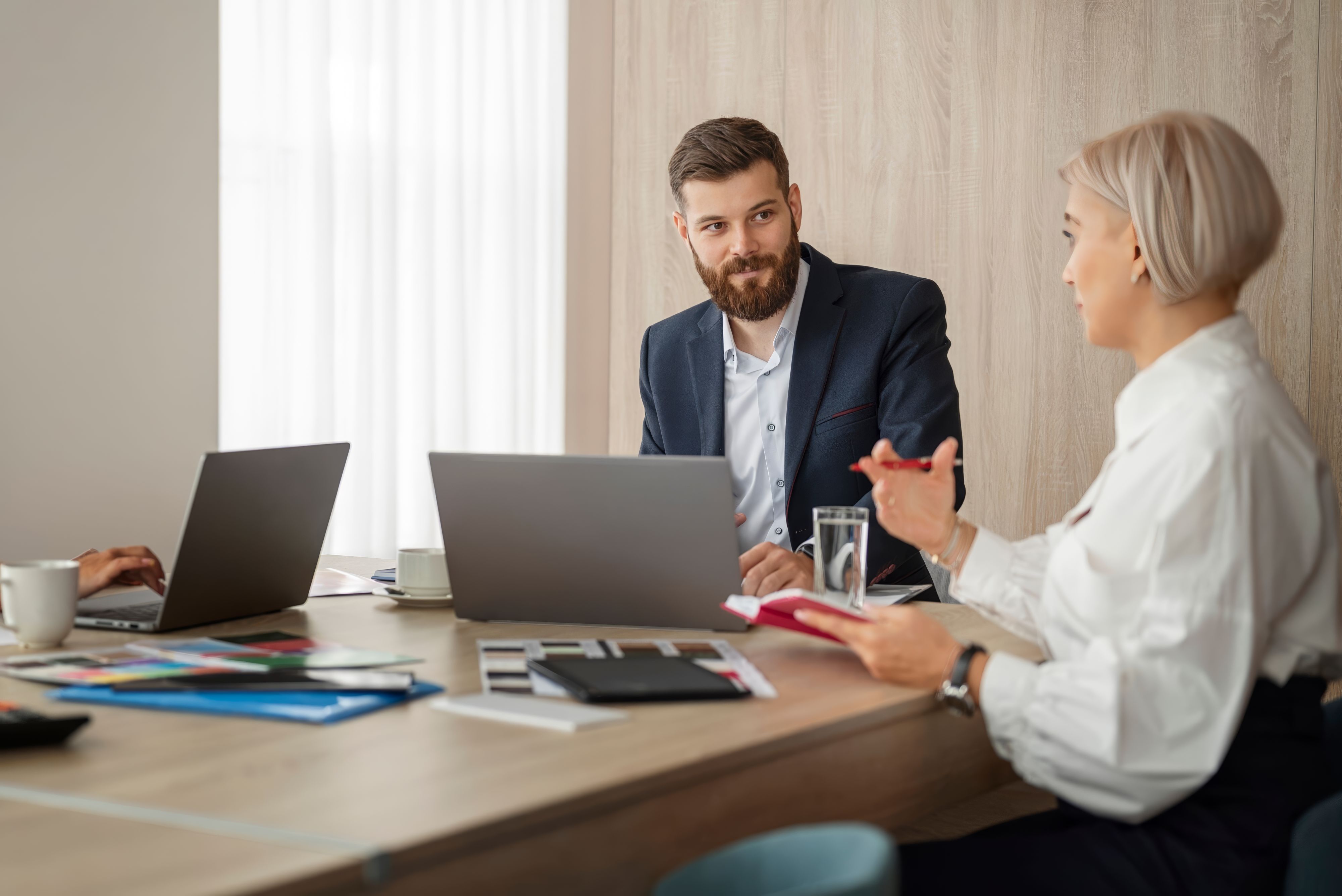 Two colleagues in a modern, sunlit office lounge engaging in a collaborative discussion