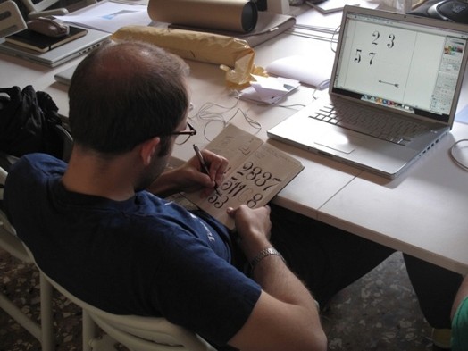 A photo of a student sketching some numbers while watching a laptop screen.