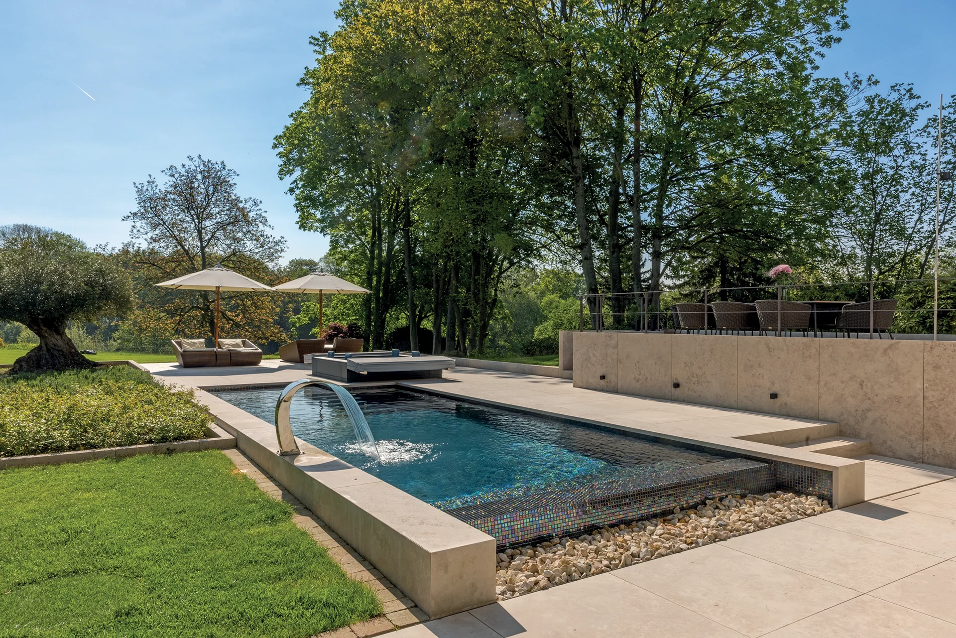 Rectangular pool with natural stone coping, sun umbrellas, and a mature garden
