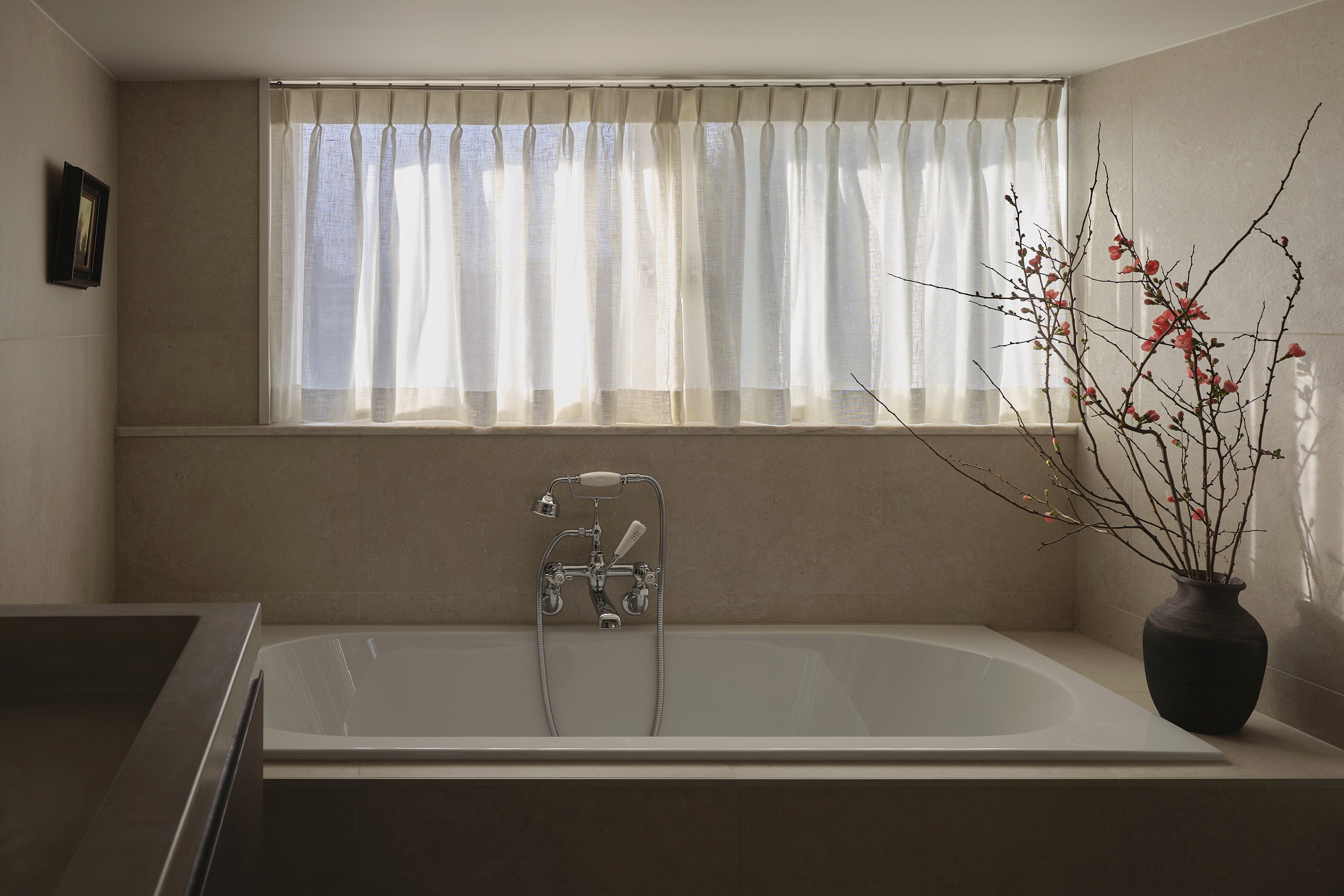 Bathroom with built-in tub, natural linen curtain, vintage chrome fixtures, and budding branches in ceramic vase