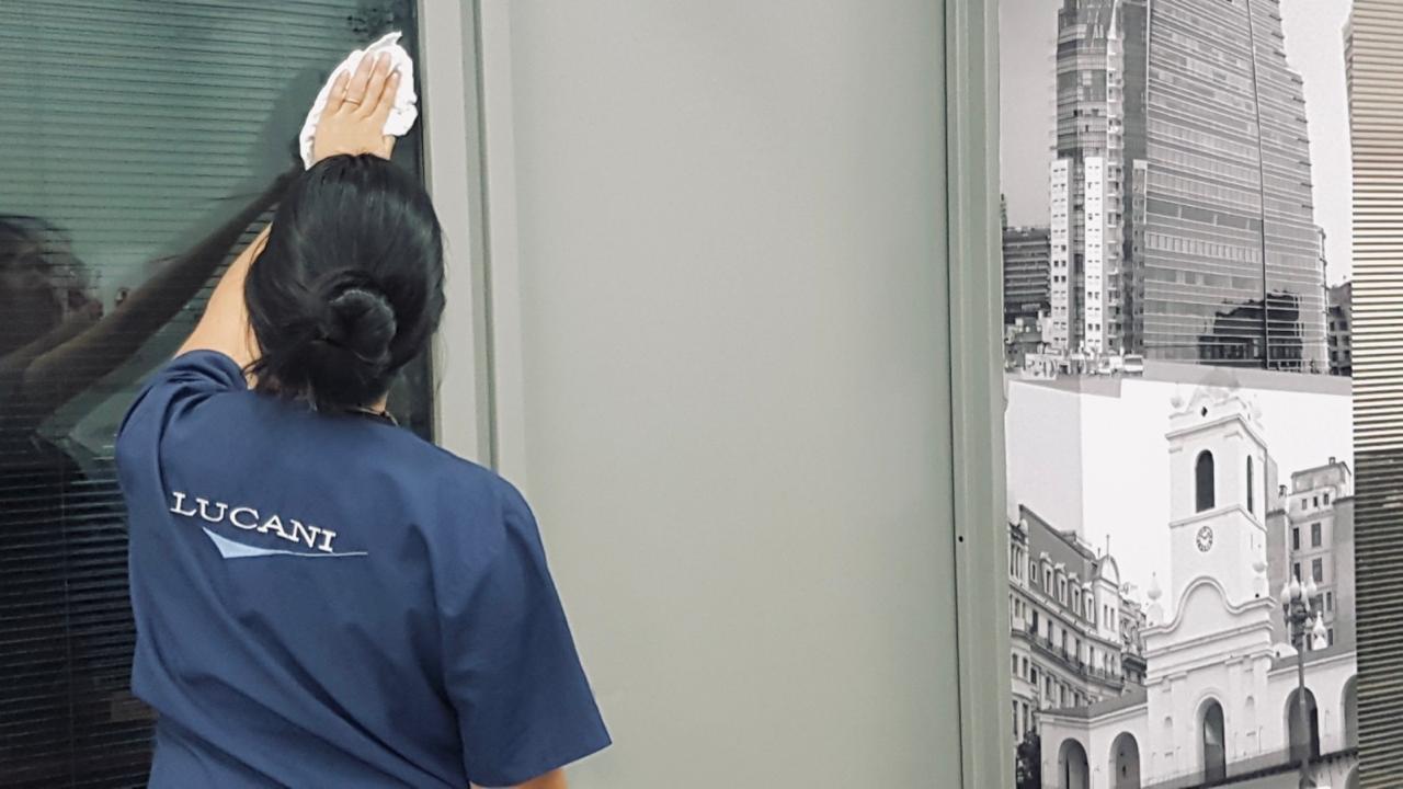 Trabajadora de limpieza con uniforme de Lucani limpiando un vidrio de gran altura