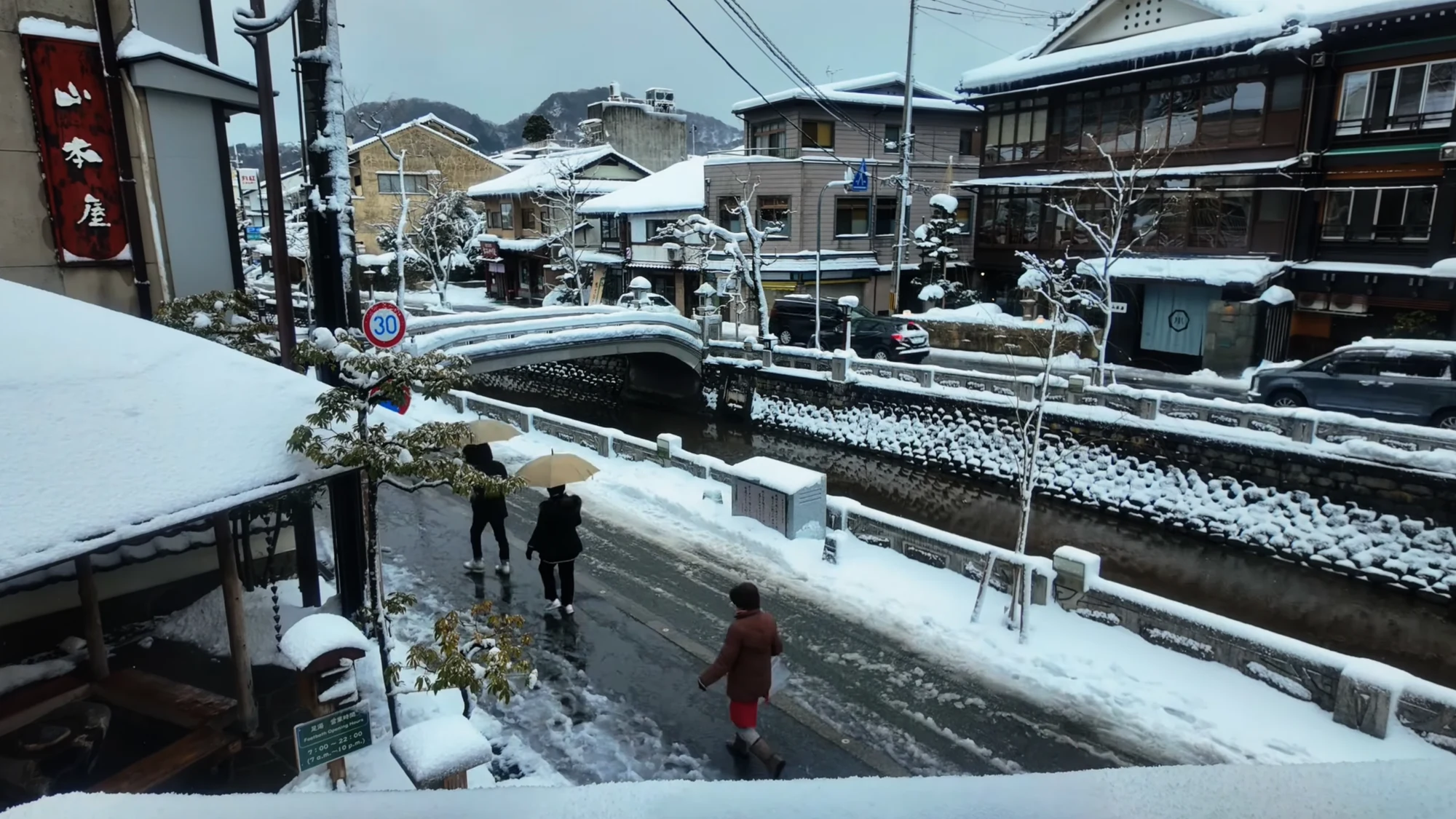 Visitors walking a snow-banked Kinosaki street lined with inns and shops.