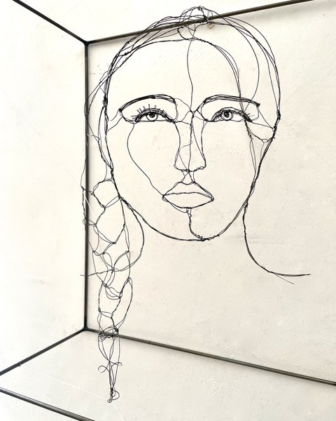 Sculpture en fil de fer représentant le visage d'une femme dans un cadre en fil de fer, vue détaillée de côté avec son ombre projeté sur le mur