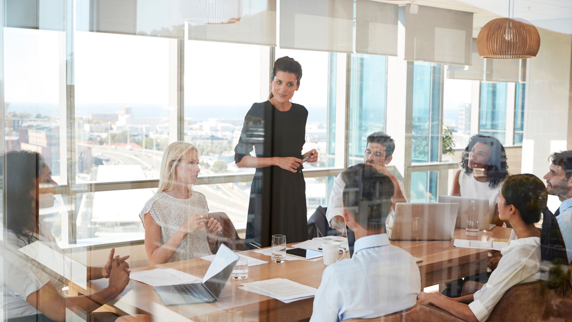 A leader standing and addressing colleagues in a glass-walled meeting room