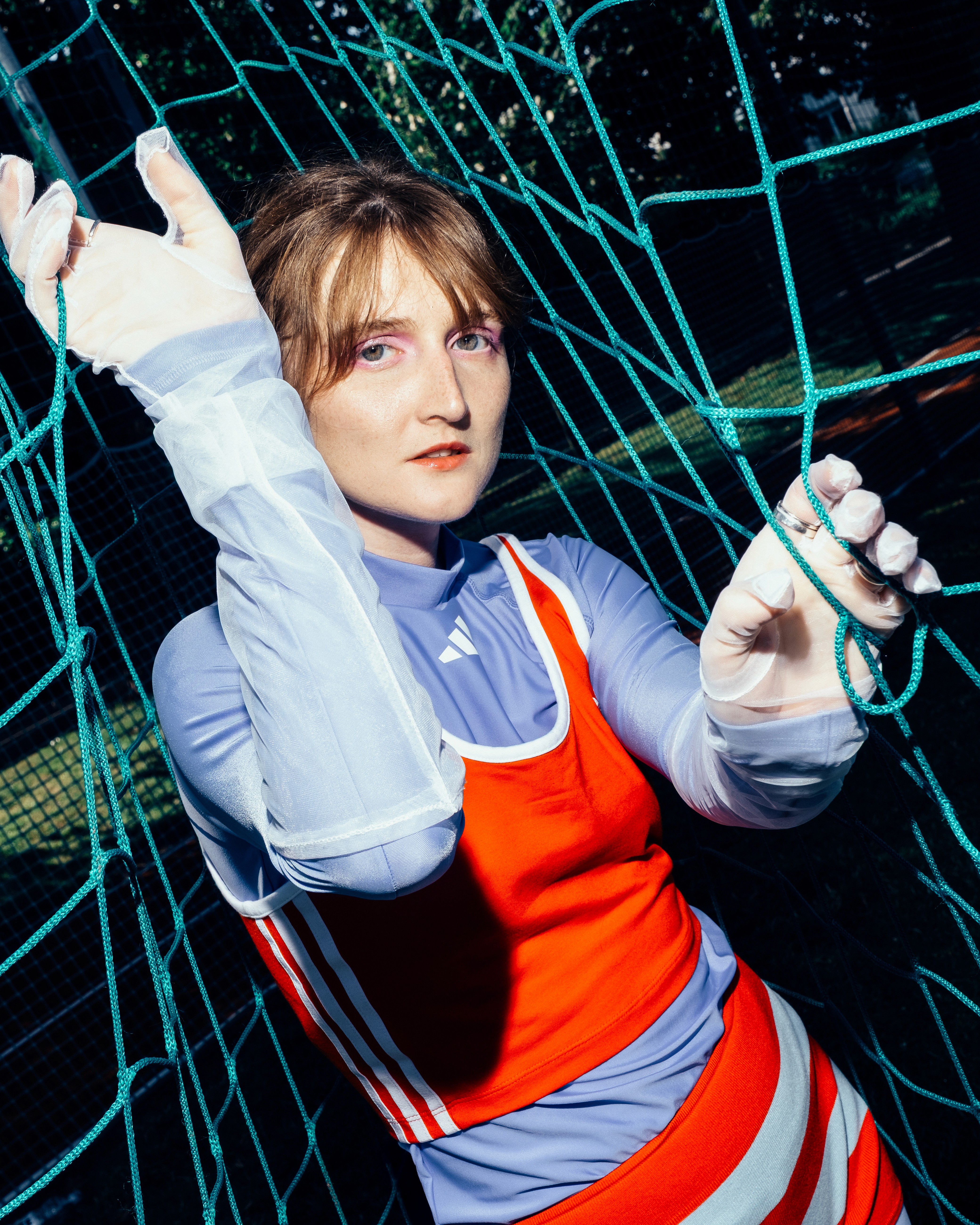 Person in sporty clothing holding onto a green net, shot in dramatic lighting.