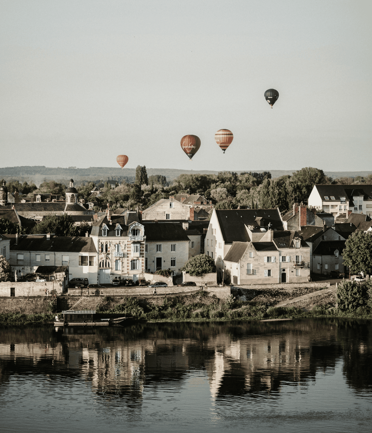 Hot-air balloons over the Loire River, reflecting in calm waters beside classic French houses.