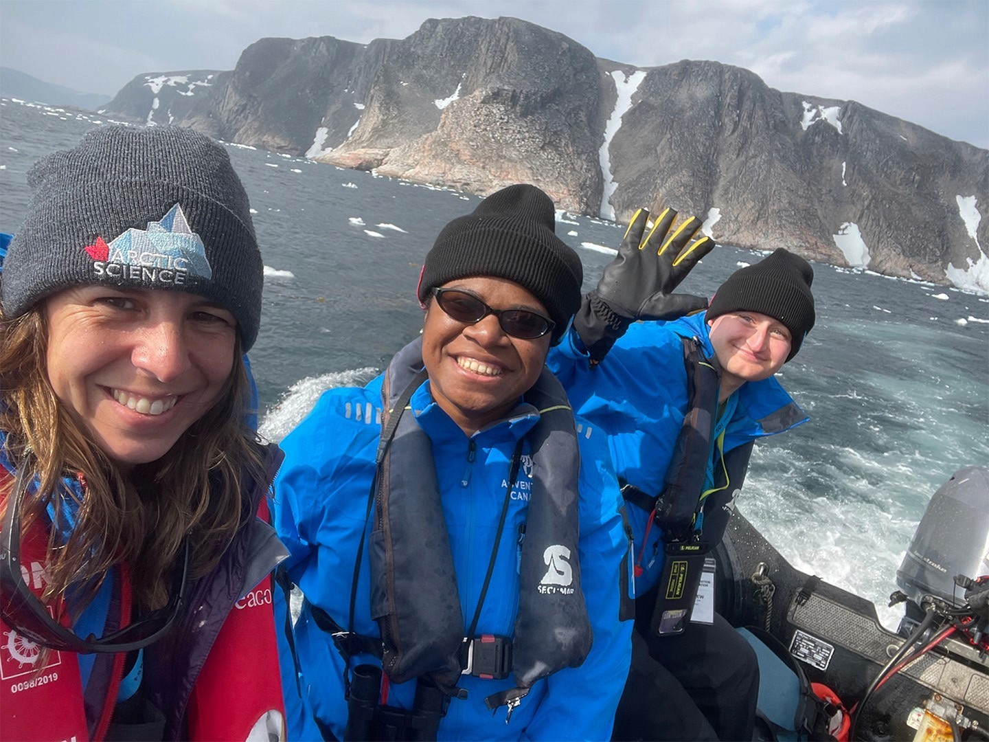 A group of students wave to the camera aboard a small boat on an expedition through Kalaallit Nunaat