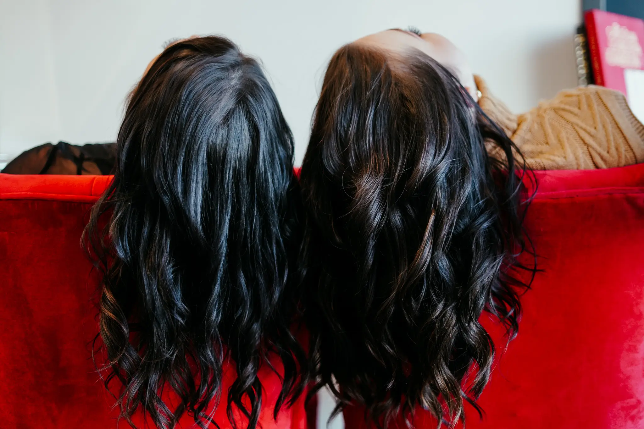 Photo of two women with their hair draped over the back of red chairs.