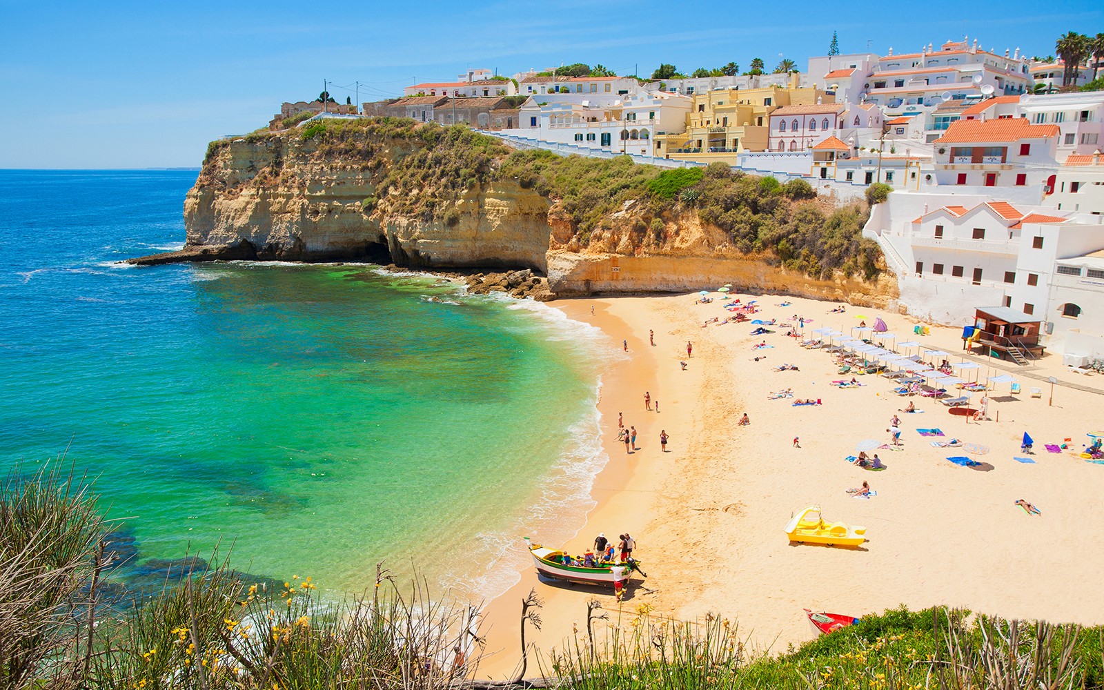 Praia de areia com barcos coloridos e falésias na Costa do Algarve, Portugal.