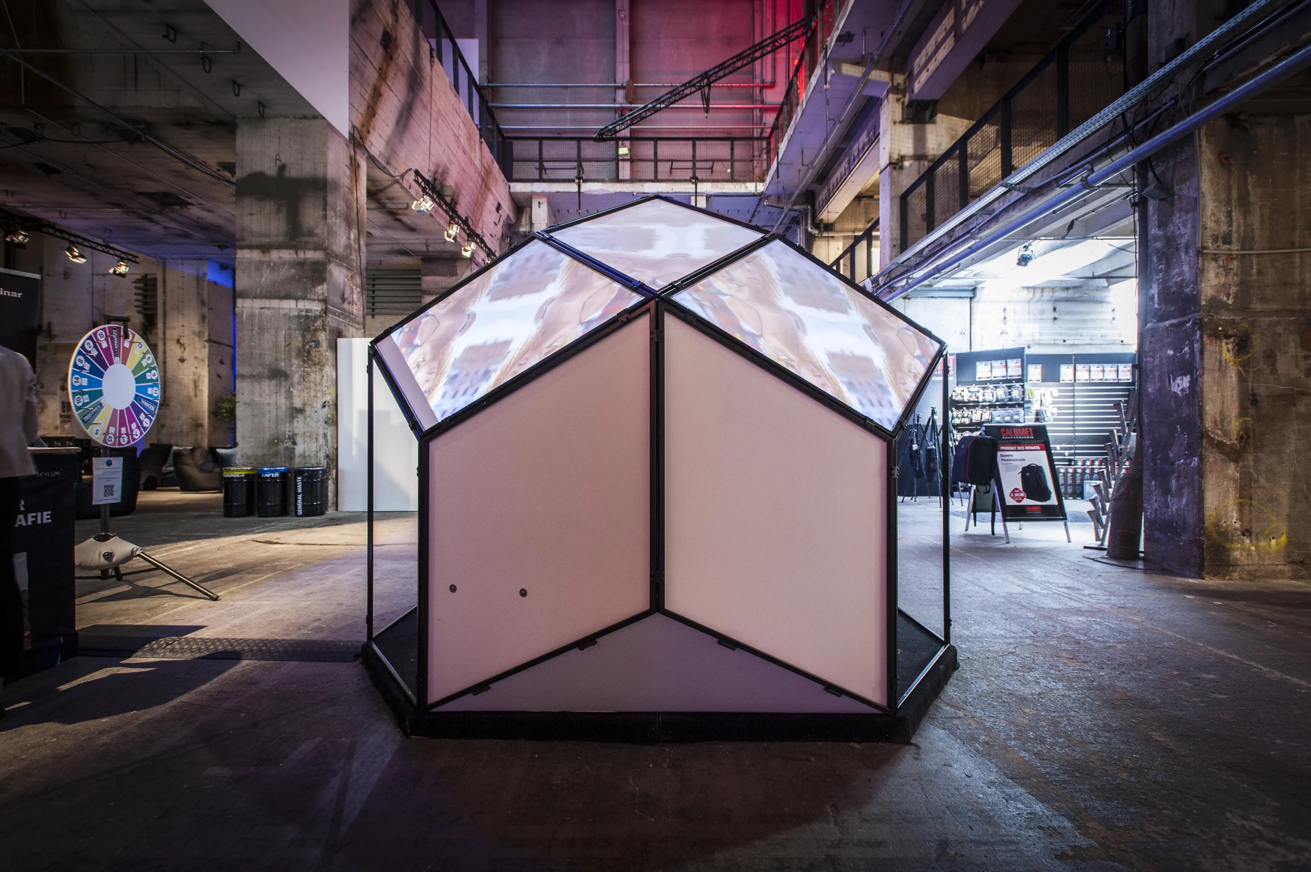 Walk-in geodesic pavilion with translucent glowing panels at BERLIN PHOTOWEEK, with a colorful spinning wheel in the background.