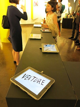 venture logo on an iPad screen sitting on a table and two persons in the back of the frame