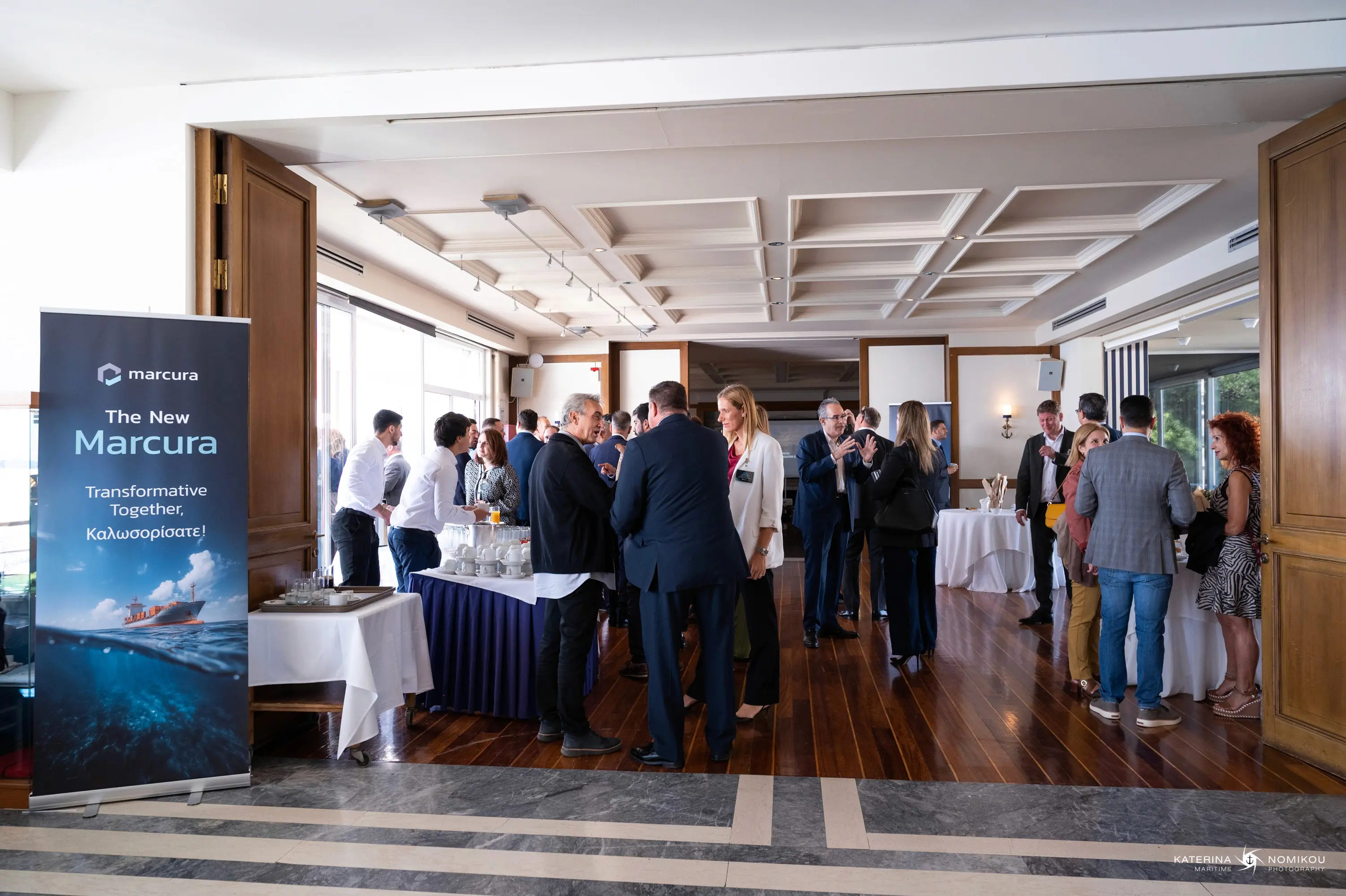 A group of people networking at an event in a spacious indoor venue with tables and banners.