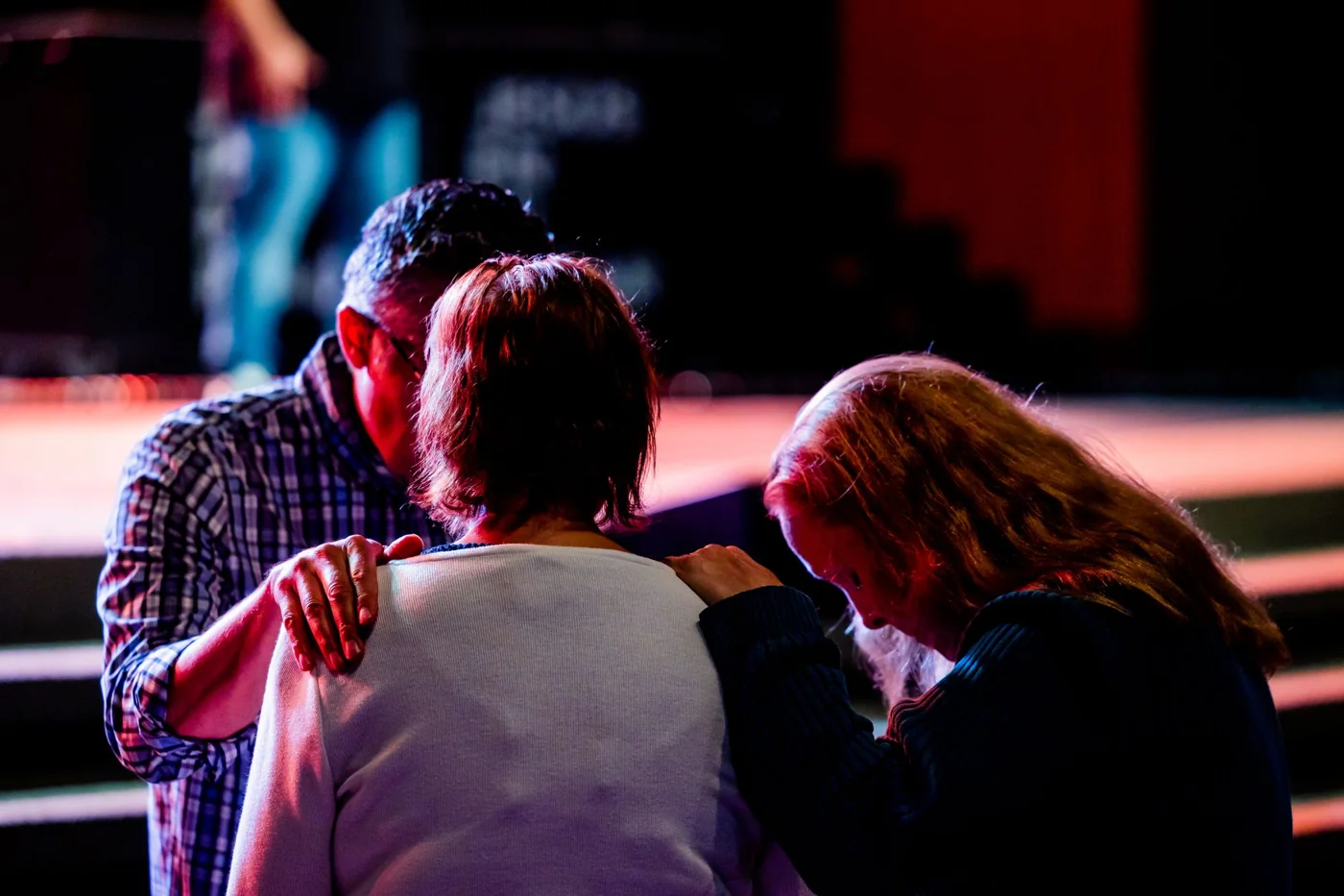Three people praying together with hands on each other’s shoulders