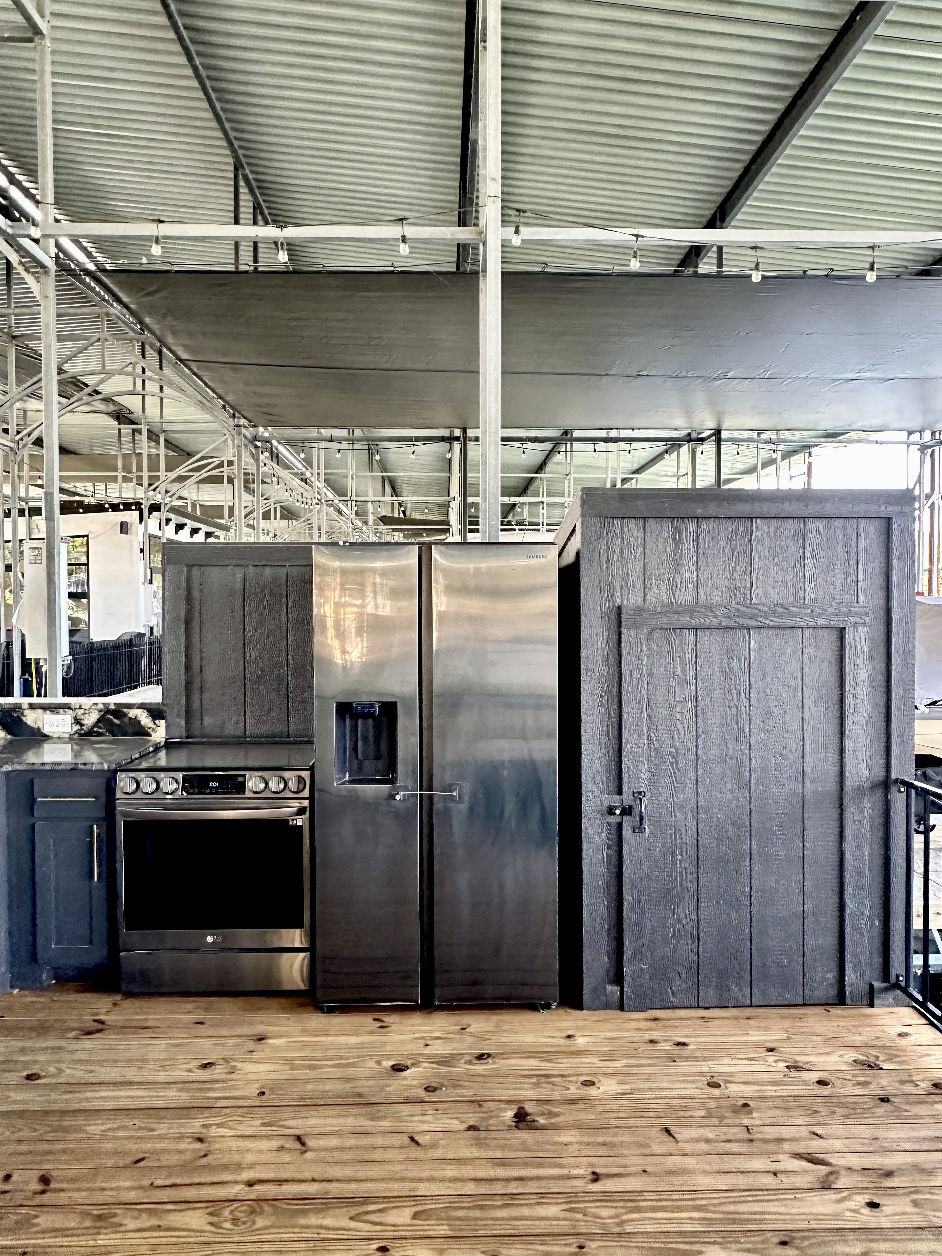 Modern industrial kitchen space featuring stainless steel appliances, including a refrigerator and oven, set against a backdrop of exposed metal beams and wooden flooring, emphasizing sleek urban design.