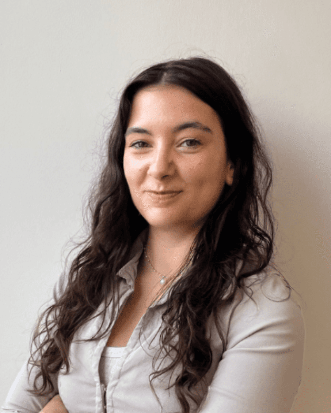 Smiling young man with curly hair, wearing a dark hoodie, against a softly lit background.