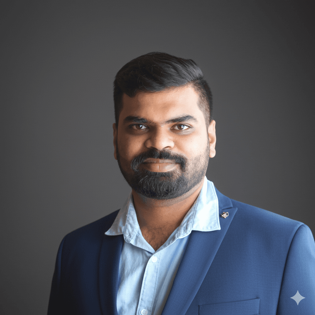 Young man in a dark suit jacket and cream sweater vest over a blue shirt with a patterned tie. Professional and confident expression, neutral background.
