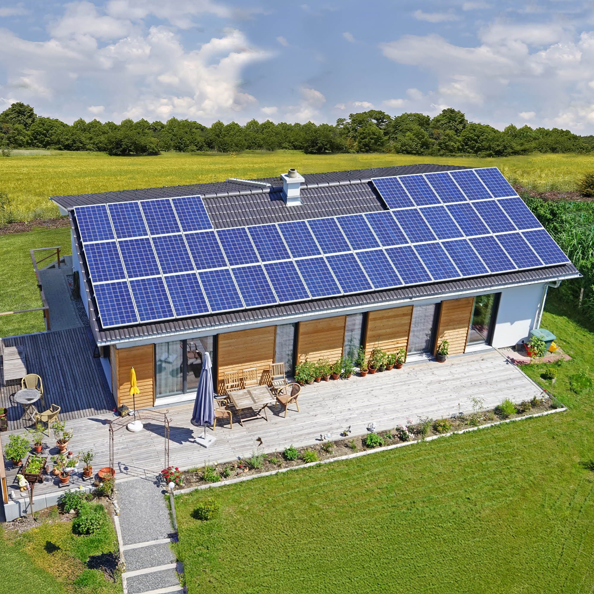 Modernhaus mit zahlreichen Solarpaneelen auf dem Dach, umgeben von grünen Rasenflächen und Feldern.