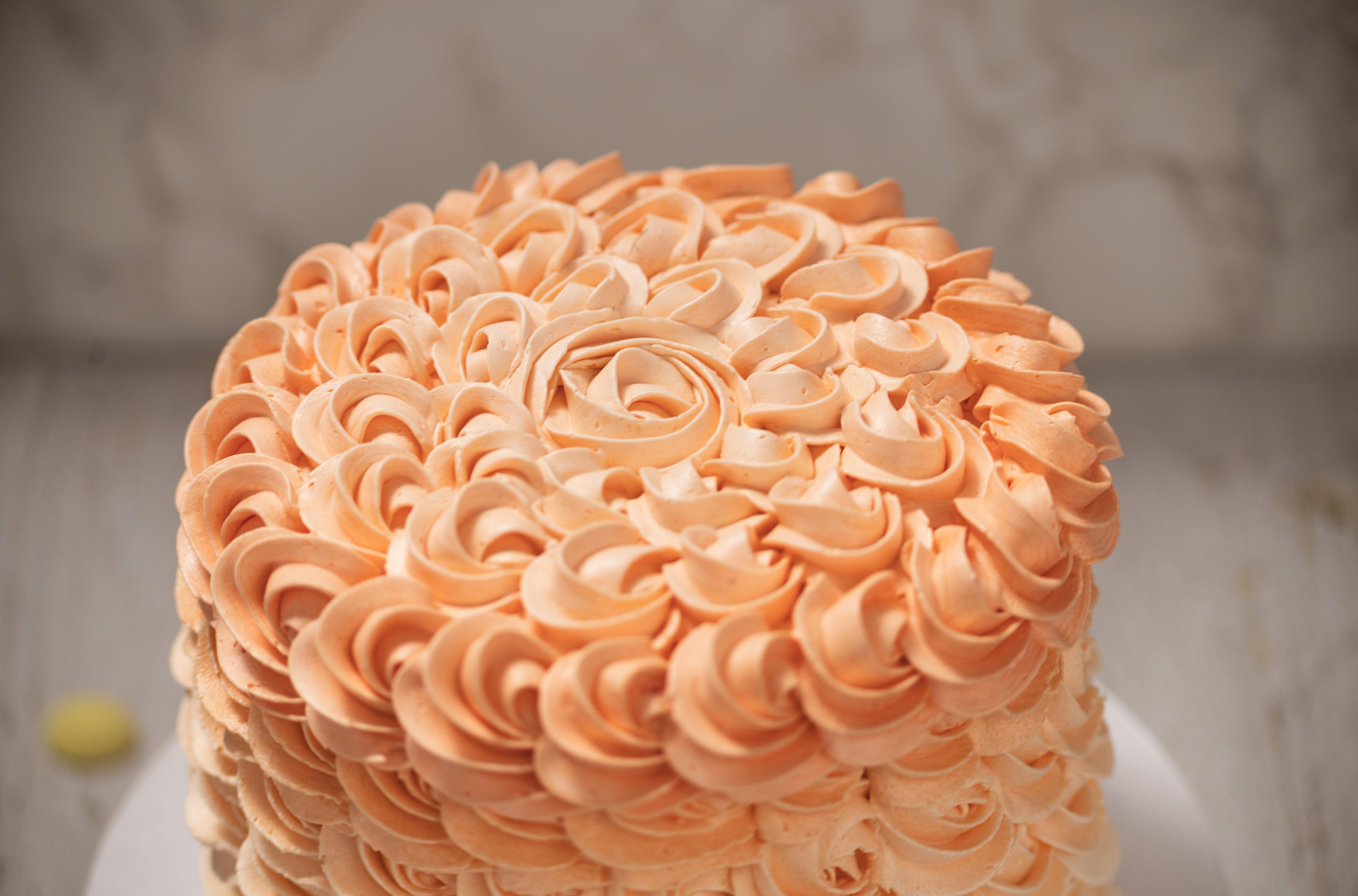 A whole round cake decorated with intricate, piped peach-colored buttercream frosting swirls, displayed on a white cake stand.