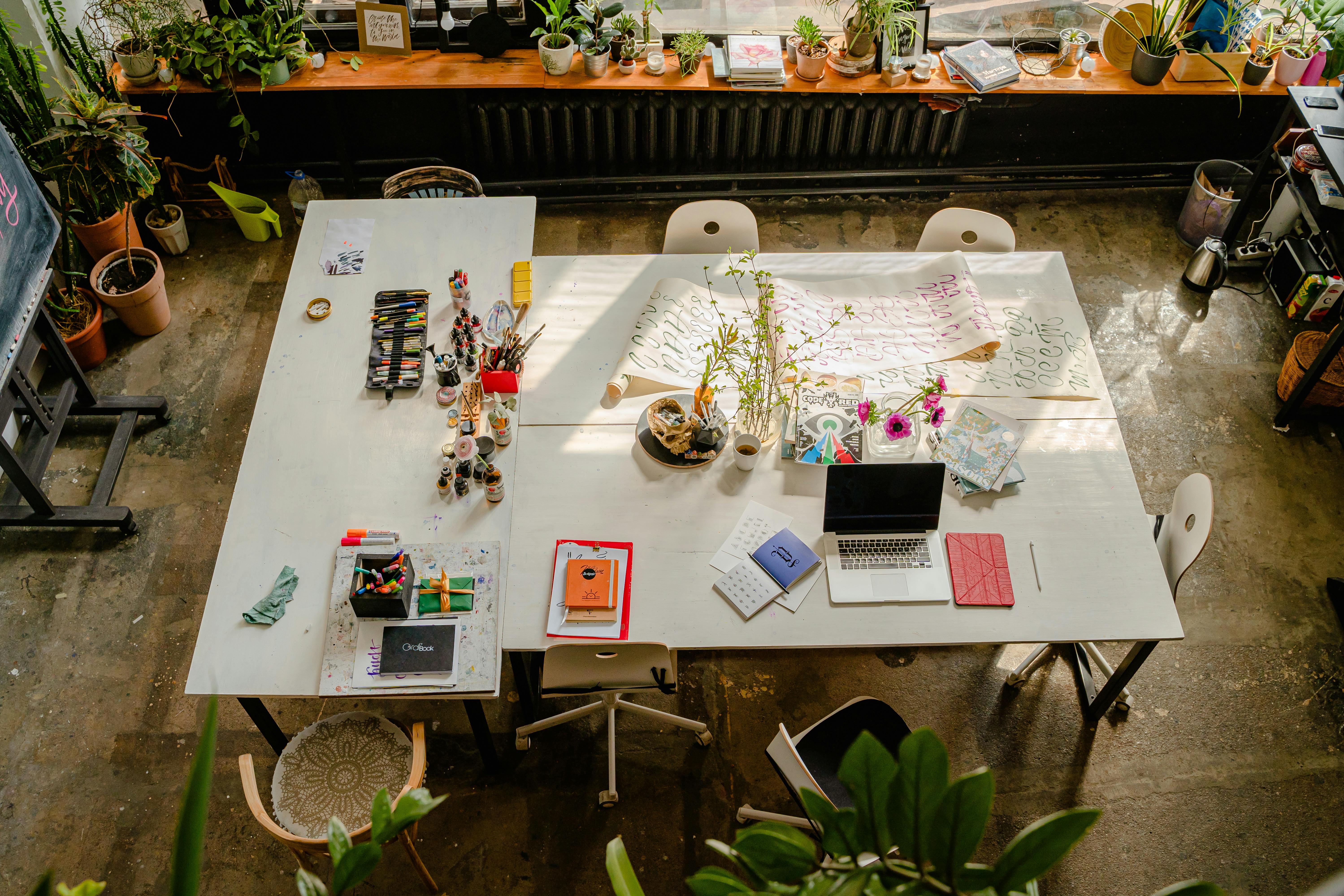 Spazio di lavoro condiviso con materiali creativi, piante e strumenti digitali, simbolo di un nuovo modo di lavorare che unisce concentrazione, autonomia e benessere quotidiano.