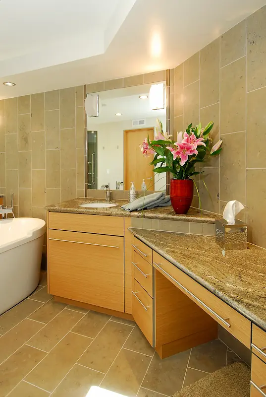 Portrait of primary bath double vanity with makeup area. Tile walls and floor. Obscured, free-standing tub. Modern kitchen with wooden cabinets, central island, hanging lights, and dark flooring. Irvine Transitional Modern. Photo by Chris Darnall.