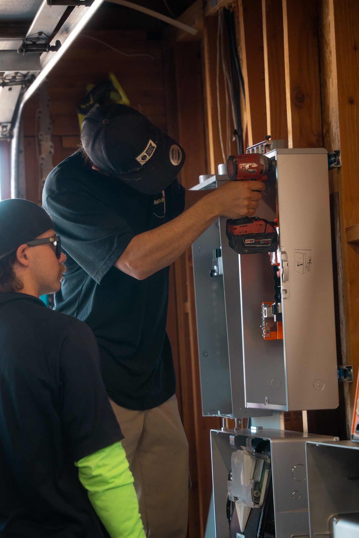Two Option One Solar electricians wiring a battery system at a garage electrical panel